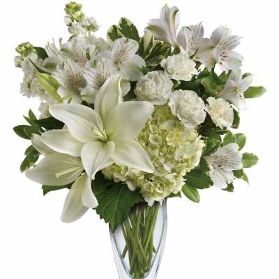 White lilies, hydrangeas, carnations, and alstroemeria arranged in a clear glass vase