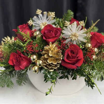 Red roses in a white bowl with gold ornaments and pinecones