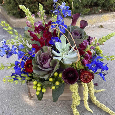 Colorful floral arrangement in a wooden box with blue, burgundy, and purple blooms