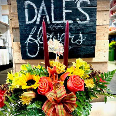 Autumn floral arrangement with sunflowers, roses, and candles in a white container