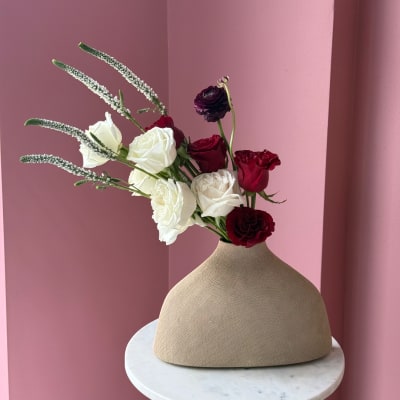 White and burgundy roses in a beige vase with tall white spikes