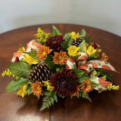 Autumn floral centerpiece with mums, pinecones, and ribbon on a table