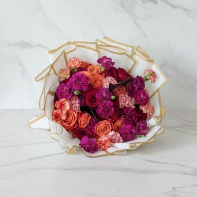 Bouquet of pink, coral, and purple roses wrapped in white paper with gold trim