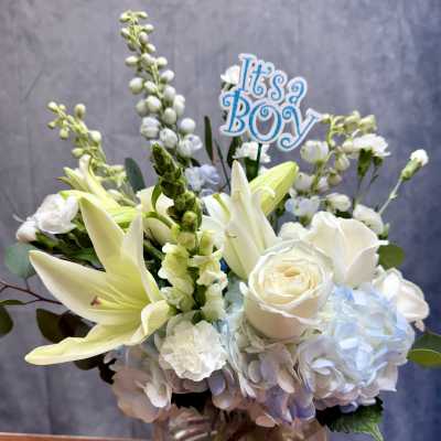 White and pale blue bouquet in a glass vase with an "It's a Boy" sign