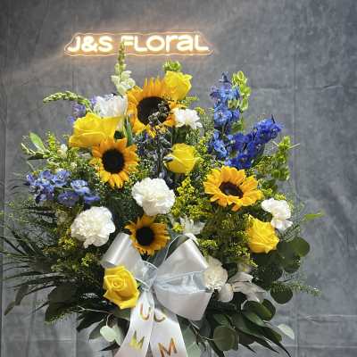 Basket arrangement with sunflowers, yellow roses, white carnations, and blue flowers