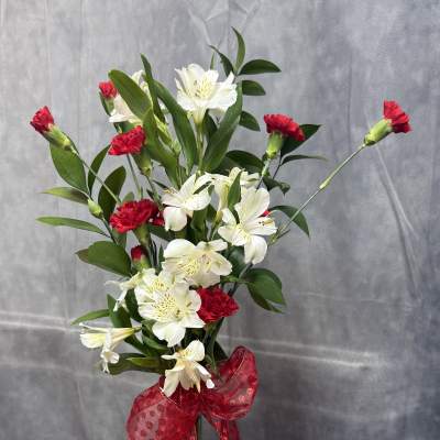 White alstroemeria and red carnations in a clear glass vase with a red bow.