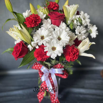 Bouquet of red roses, white daisies, and red carnations in a glass vase