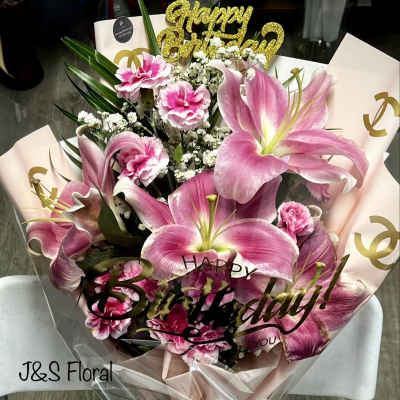 Pink lilies and carnations in a wrapped bouquet with a birthday topper
