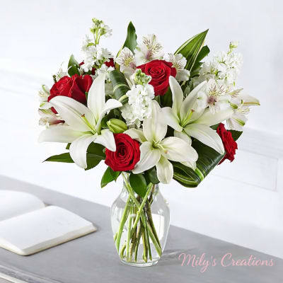Red roses and white lilies with curled green leaves arranged in a clear glass vase