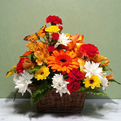 Basket arrangement of orange, red, yellow, and white flowers with a butterfly decoration