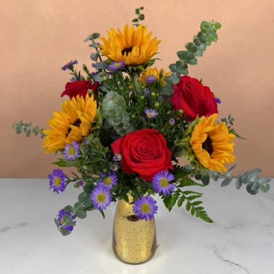 Bouquet of red roses, sunflowers, and purple daisies in a gold vase