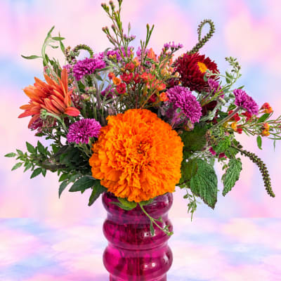 Bright mixed bouquet with orange and purple flowers in a pink glass vase