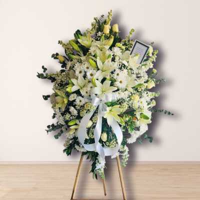White floral standing spray on an easel with a ribbon bow