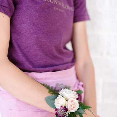 Person wearing a small wrist corsage with pale roses and purple flowers