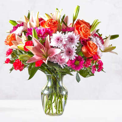 Mixed bouquet of pink and orange flowers in a clear glass vase