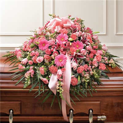 Pink floral casket spray with ribbon on a wooden coffin