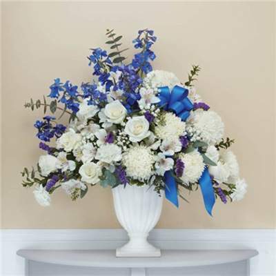 White and blue floral arrangement in a white urn vase with ribbon