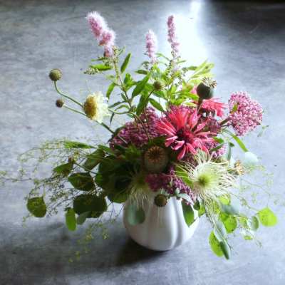 Loose garden-style arrangement of pink and white wildflowers in a white ceramic vase