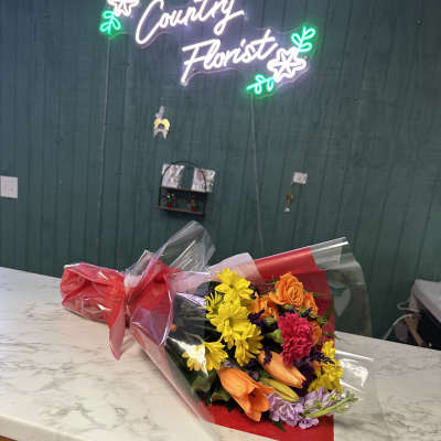 Wrapped bouquet with yellow daisies, orange roses, and pink carnations