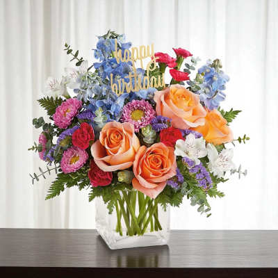 Mixed bouquet of roses, daisies, and blue flowers in a clear vase
