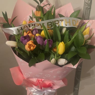 Bouquet of multicolored tulips wrapped in pink paper with a birthday ribbon