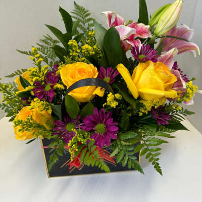 Bouquet of yellow roses, pink lilies, and purple daisies in a gift box