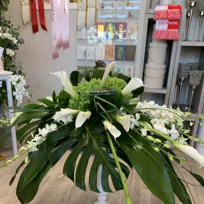 White calla lilies and orchids arranged in a white pedestal vase