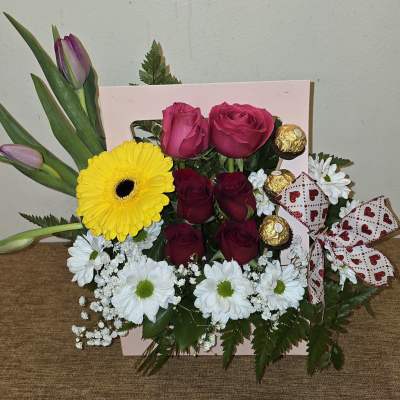 Bouquet of pink roses, a yellow gerbera daisy, and white daisies with chocolates and a ribbon