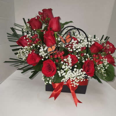 Red roses with white baby's breath in a black box, accented by butterflies and a red ribbon.