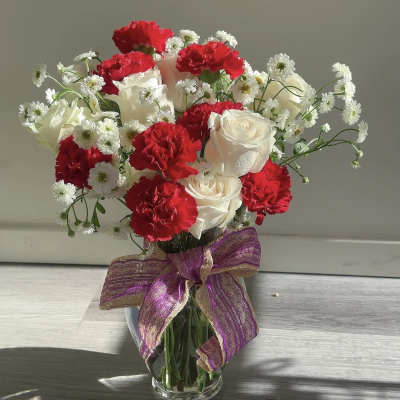 Bouquet of red carnations and white roses in a glass vase with a purple ribbon