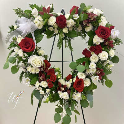 Heart-shaped floral wreath with red and white roses on a black stand