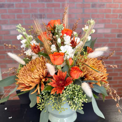 Orange roses and chrysanthemums in a white vase with dried accents