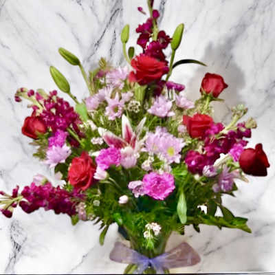 Mixed bouquet of pink and red flowers with a purple ribbon