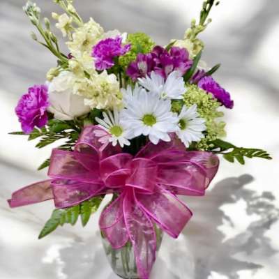 Bouquet of white daisies and pink flowers in a glass vase with a pink ribbon