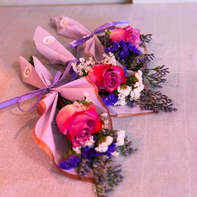 Three small pink rose bouquets wrapped in pastel paper with purple ribbon