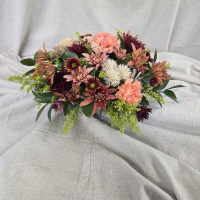 Low arrangement of peach carnations and burgundy chrysanthemums on a neutral draped backdrop