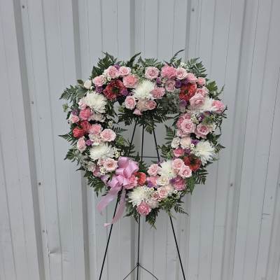 Heart-shaped standing wreath of pink and white flowers with a pink bow on an easel.