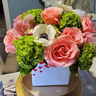 Pink roses and a white anemone in a white box with green hydrangeas