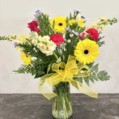 Bouquet of yellow gerbera daisies, red roses, and white snapdragons in a glass vase