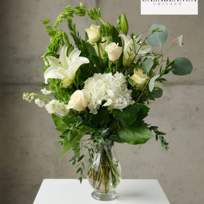 White lilies and roses in a clear glass vase with greenery