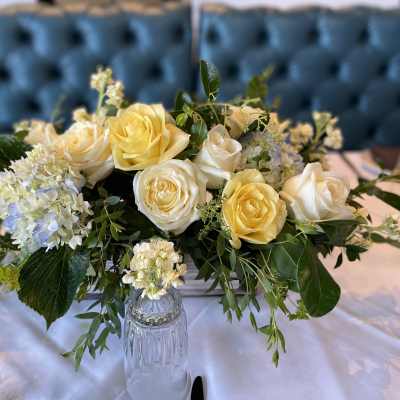 Low arrangement of yellow and cream roses with white hydrangeas on a set table.