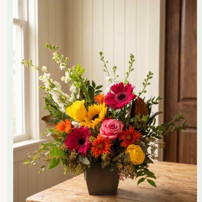 Mixed bouquet in a dark vase with roses, gerbera daisies, and sunflowers