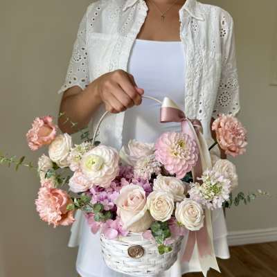 Woman holding a white basket of pink and cream flowers with ribbon