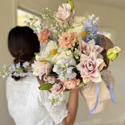 Bride holding a pastel bouquet with lilies, roses, and blue flowers