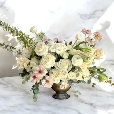 Cream and blush floral arrangement in a gold pedestal vase