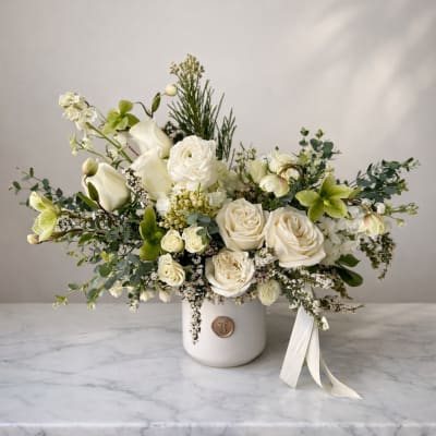 White floral arrangement in a white vase with a ribbon