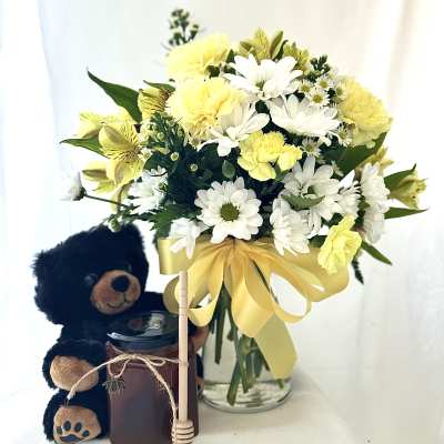 Yellow and white bouquet in a glass vase with a teddy bear and candle