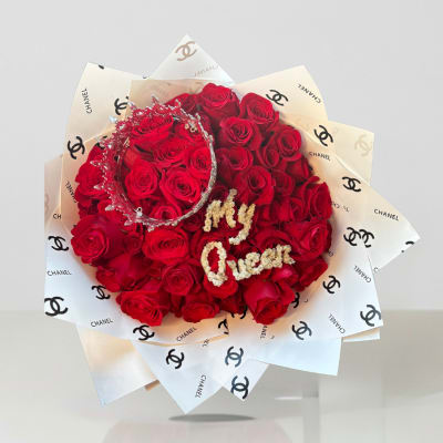 Red rose bouquet wrapped in Chanel-logo paper with a jeweled crown
