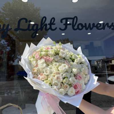 Large bouquet of white and blush roses wrapped in white paper with a pink ribbon