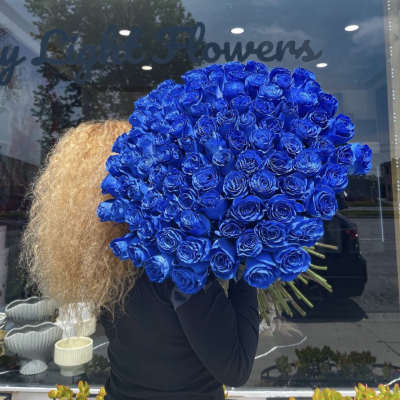 Large bouquet of vivid blue roses held in front of a shop window